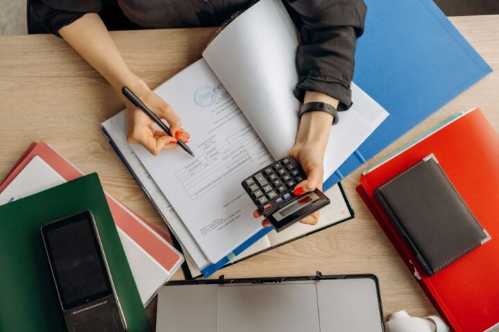 Bàn tay ghi chép vào sổ kế toán bên cạnh máy tính cầm tay